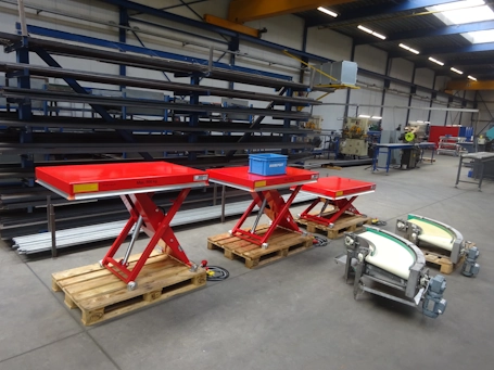 Je ziet drie rode heftafels staan, van groot naar klein, met ook 2 bandbochten in beeld. De foto is genomen in de werkplaats van Beerepoot. Er staan een blauw Beerepoot kratje op de middelste rode heftafel.