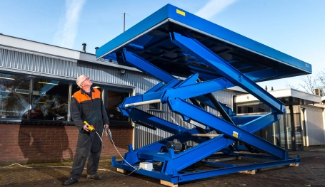 Je ziet een grote blauwe heftafel van Beerepoot buiten staan die bediend wordt door een monteur van Beerepoot in een blauw pak met oranje details.
