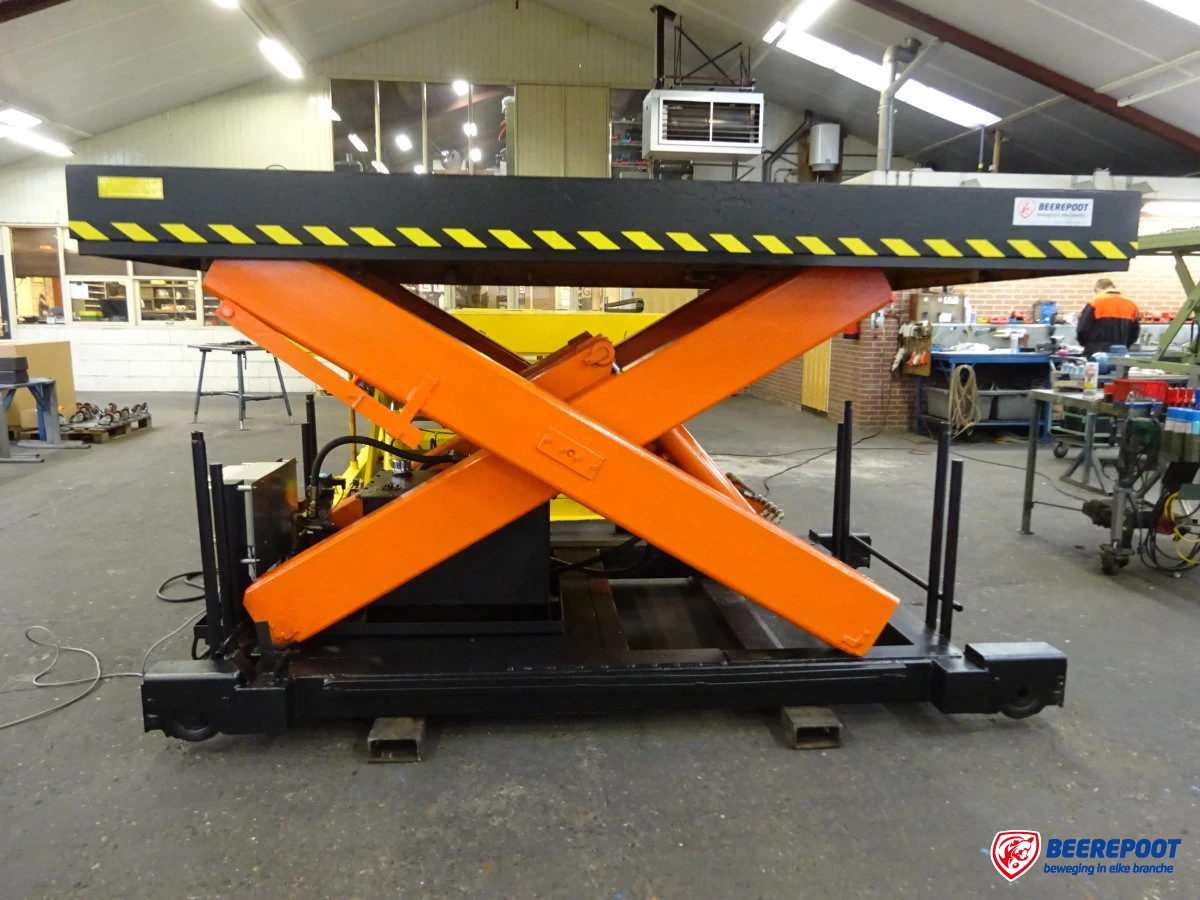 Je ziet een grote oranje heftafel van Beerepoot die in de werkplaats van Beerepoot staat.