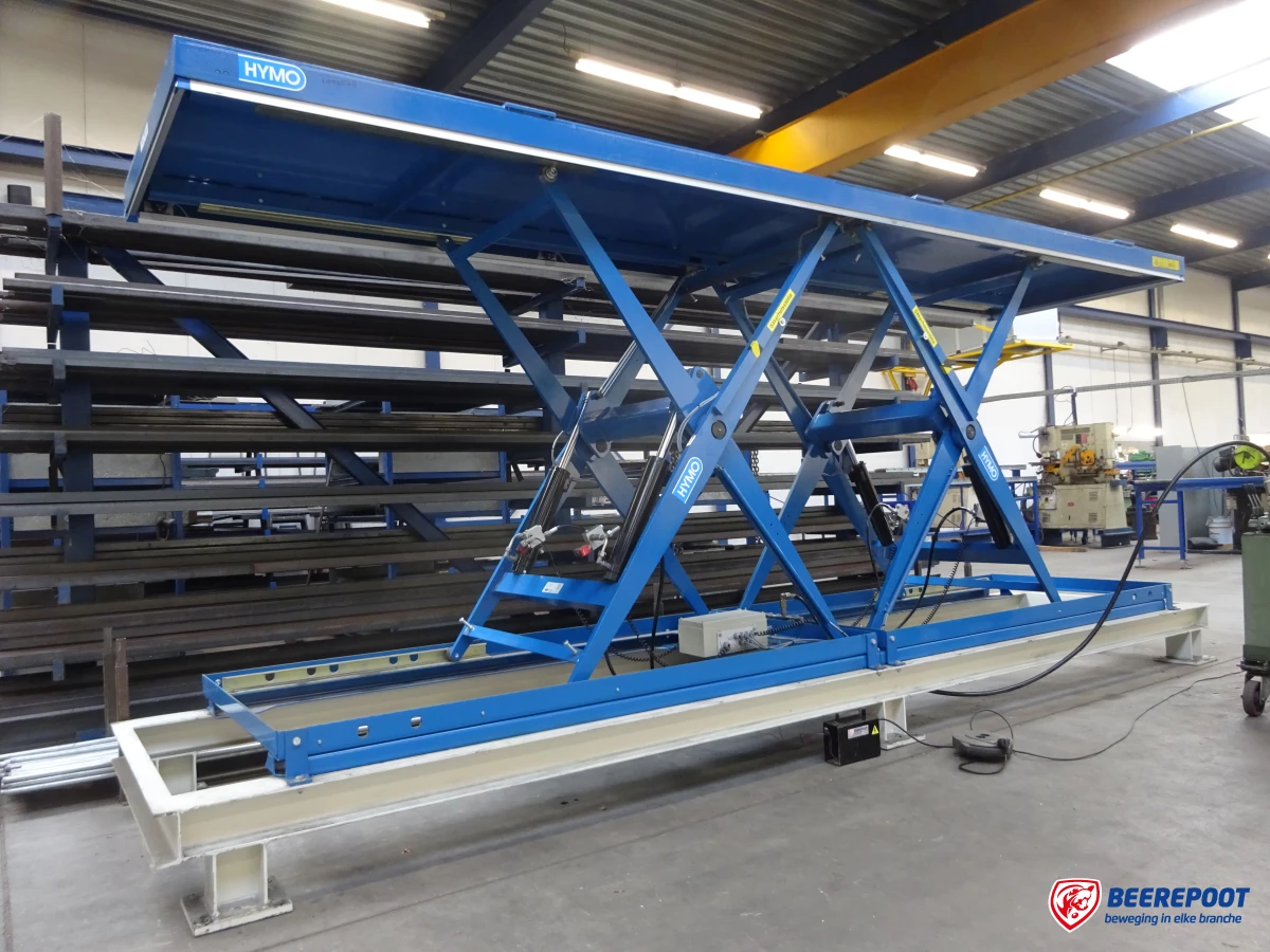 Je ziet een grote blauwe horizontaal dubbelscharende heftafel van Beerepoot. De heftafel staat in de werkplaats van Beerepoot.