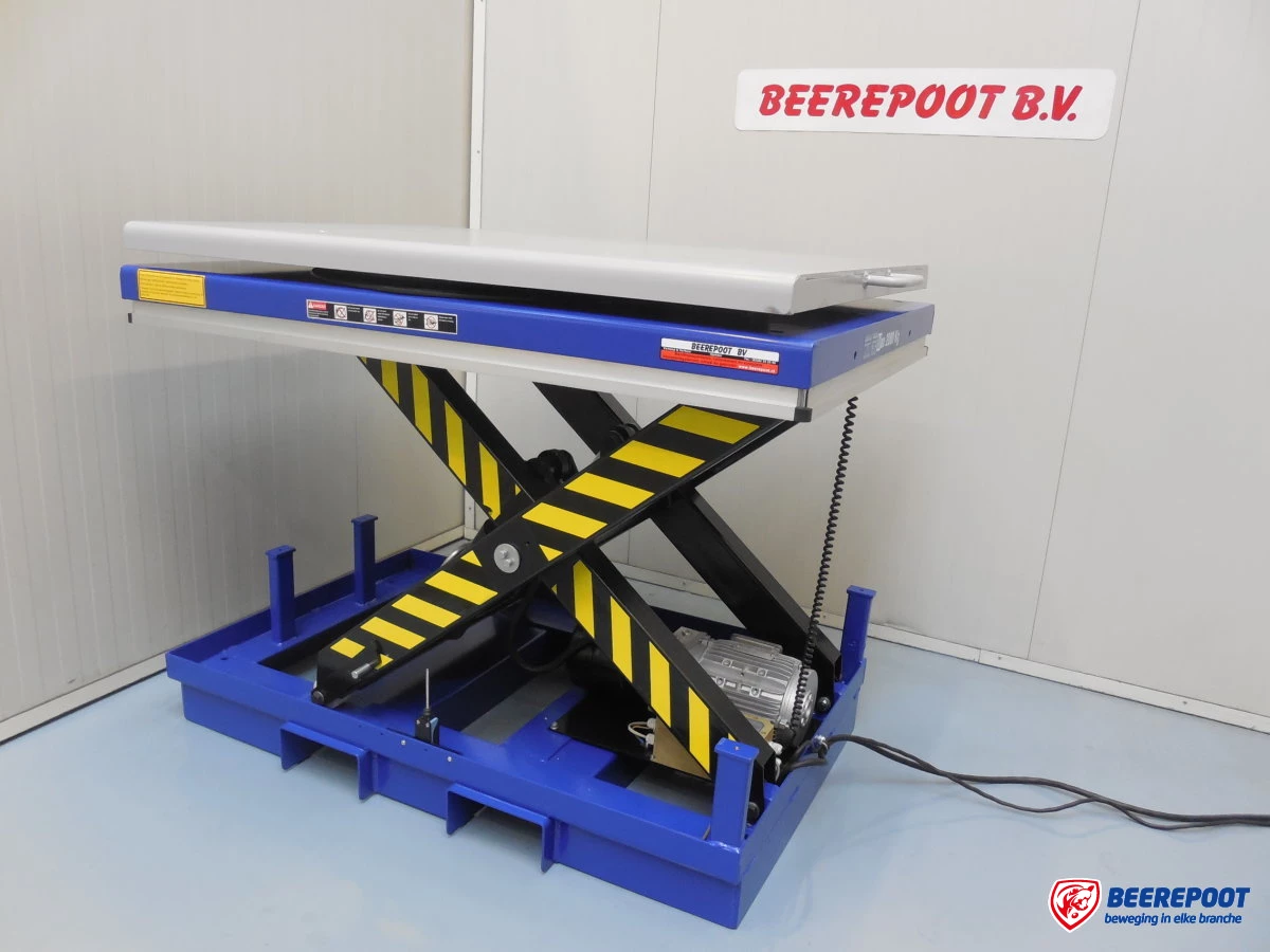 Je ziet een nieuwe blauwe heftafel van Beerepoot met zwart/ gele scharen. De heftafel staan in een voorraadhal van Beerepoot.